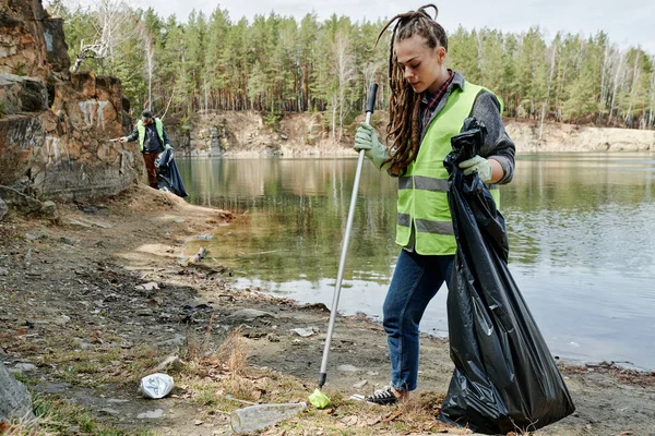 地球の日に湖畔の清掃イベントに参加する若い女性 — ストック写真