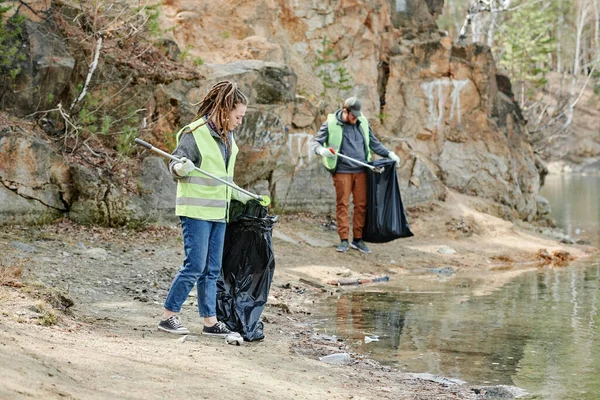 ゴミ拾いの道具を使って湖畔を掃除する若者たち — ストック写真