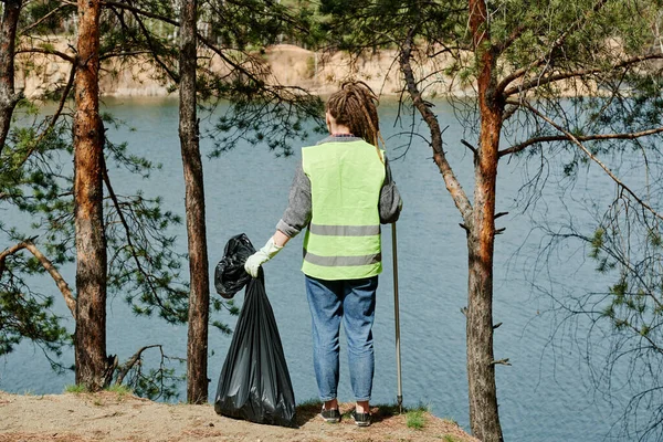 若いです女性でネオンベスト保持ビニール袋とともに彼女が収集し 池を見て — ストック写真