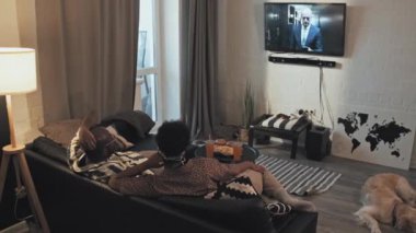 Genç Afro-Amerikan çiftin oturma odasında oturup, akşamları televizyon izlediği, köpeklerin yerde uyuduğu yüksek açı.