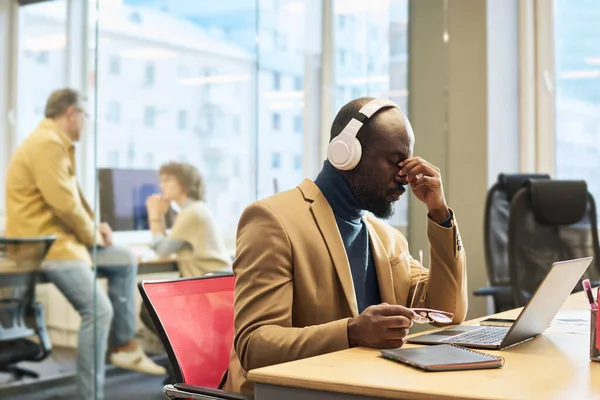 Młody Zmęczony Biznesmen Słuchawkach Siedzący Przed Laptopem Miejscu Pracy Mający — Zdjęcie stockowe