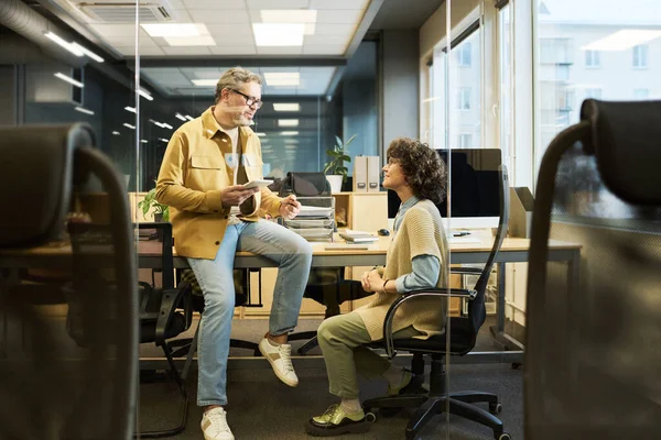 自信成熟的男性经理在开会时穿着便服与年轻的女性同事交谈 同时使用带有图形数据的平板电脑 — 图库照片