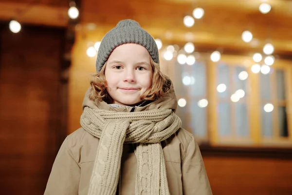 穿着贝尼 针织羊毛衫和保暖夹克的可爱小男孩 站在带装饰灯的茅屋旁边看着相机 — 图库照片