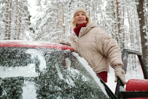 快乐成熟的金发女人 穿着温暖的冬季夹克 头戴针织贝尼帽 头戴羊毛衫 旅行时站在敞开的车门旁 — 图库照片