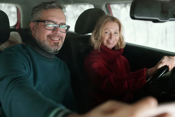 戴着眼镜的快乐而成熟的男人 穿着温暖的绿色毛衣 用智能手机向他的妻子展示当地地图 一边开车一边手握方向盘 — 图库照片
