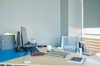Gri duvar ve büyük pencerenin yanında duran ofis yöneticisi veya tasarımcı mobil cihazlar ve diğer malzemeler
