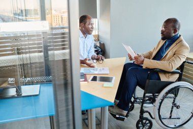 Kendine güvenen patron, tekerlekli sandalyedeki astının raporunu dinliyor, yorumluyor, yöneticiye sorular soruyor ve ona danışıyor.