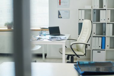 Beyaz deri koltuk ve malzemelerle dolu masadan oluşan iş yeri olan hekimlik ya da diğer uzmanların muayenehanesinin bir parçası.