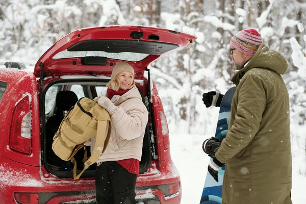 快乐的老年妇女 背着背包 背着雪板看着丈夫 从汽车行李箱中取出行李 — 图库照片