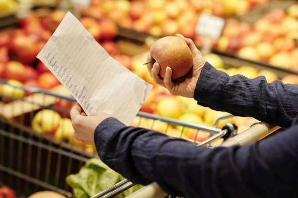 ショッピングリストと新鮮な熟した赤いリンゴを保持しながら 食料品部門で果物を選択して成熟した女性の顧客の手のクローズアップ — ストック写真