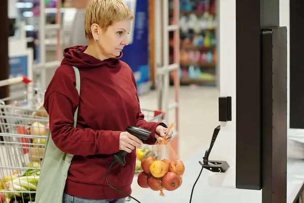スーパーマーケットで新鮮な熟したリンゴのパックをスキャンしながら 製品の価格で画面を見てカジュアルウェアでブロンド成熟した女性の消費者 — ストック写真
