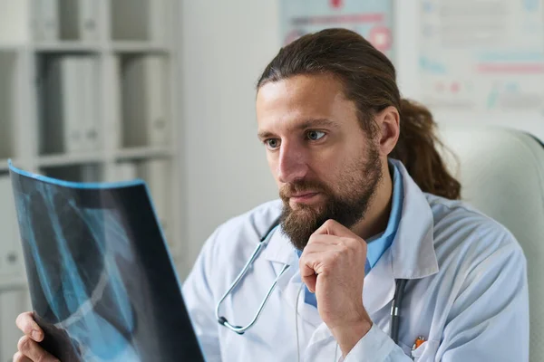 医務室に座って診断を考えながら 目の前に肺のX線画像を持っている真剣な男性放射線科医 — ストック写真