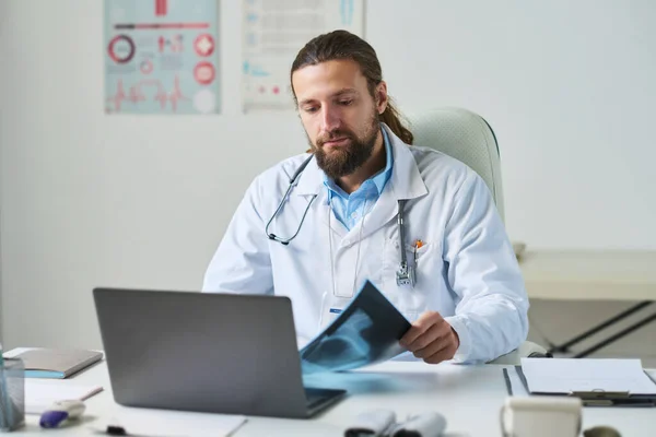 診療所の医療事務所でオンライン患者に相談しながら X線を見て研究室のコートの男性一般開業医を自信を持って — ストック写真