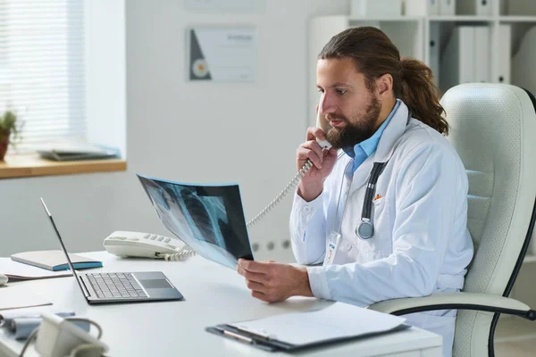 Självsäker Manlig Kliniker Labbrock Tittar Röntgenresultat Patienten Telefonkonsultation Medan Sitter — Stockfoto