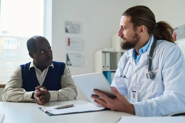 Ung Läkare Med Tablett Tittar Afroamerikanska Senior Manliga Patienten Och — Stockfoto