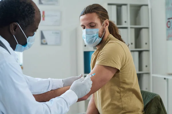 Зрілий Клініцист Захисній Масці Робить Єкцію Вакцини Молодому Пацієнту Сидячи — стокове фото