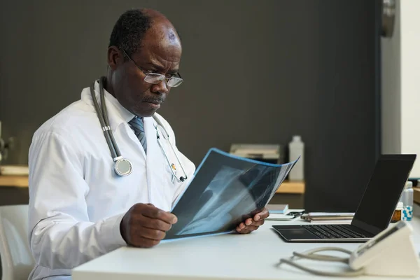 Poważny Afro Amerykański Radiolog Patrząc Wynik Prześwietlenia Płuc Podczas Siedzenia — Zdjęcie stockowe