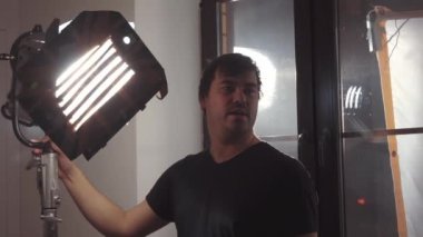 Kafkas erkek aydınlatma teknisyeninin göğüs yukarı, sahne ışıklarını kapalı mekan prodüksiyon setine ayarlıyor.