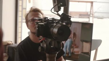 Gözlüklü genç adam, gündüz vakti profesyonel kamera kullanarak ticari videolar çekiyor.