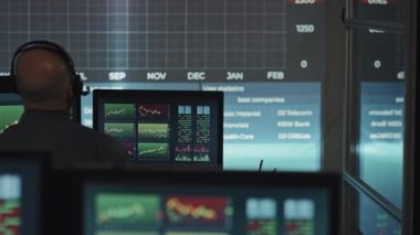 Kulaklık takan, menkul kıymetler ve döviz borsaları ile çalışan, borsa bürosundaki masasında oturan, tanınmamış, olgun bir adamın arka görünüşü.