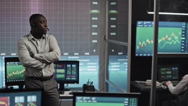 深夜时分 年轻自信的黑人股票交易专家头戴耳机 手挽手站在办公室里 配备各种电脑的画像 — 图库视频影像