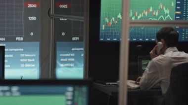 Akşam geç saatlerde ofis masasında oturan tanınmayan genç adam hisse senedi veya kripto döviz alım-satım istatistikleriyle telefon görüşmesi yapıyor.