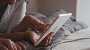 Siyah ve Kafkas kız arkadaşlarının yakın plan çekimleri. Yatak odasında dinleniyorlar. İnternette dijital tabletten bir şeyler izleyip sohbet ediyorlar.