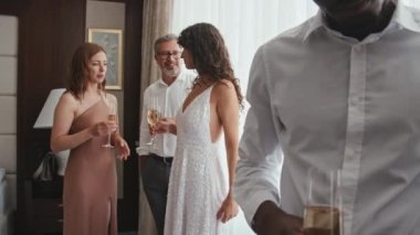 Uzun kıvırcık saçlı beyaz bir gelin, ailesi ve arkadaşları ellerinde kadehlerle evde toplanmış düğün öncesi gevşeyip sohbet ediyorlardı.