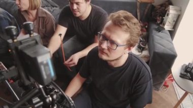 Gözlüklü genç adamın gündüz vakti profesyonel video kamerayla çekim yaptığını ve yönetmenle konuştuğunu tepeden tırnağa görüyoruz.