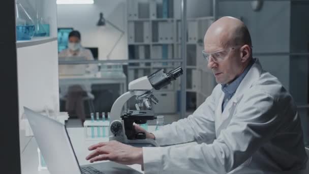 Modern Laboratuvarda Mikroskop Kullanan Masa Başında Bilgisayar Kullanan Beyaz Önlüklü — Stok video