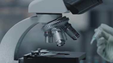 Tanınmayan teknisyenlerin mikroskop camına sıvı damlatırken yakın çekim yan görüntüsü.