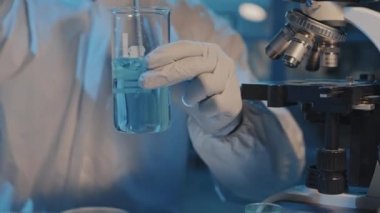Beyaz tehlikeli madde giysisi ve solunum cihazıyla laboratuvarda oturmuş test tüpünde tehlikeli kimyasalları karıştıran siyah bir bilim adamını yukarı çekmek.