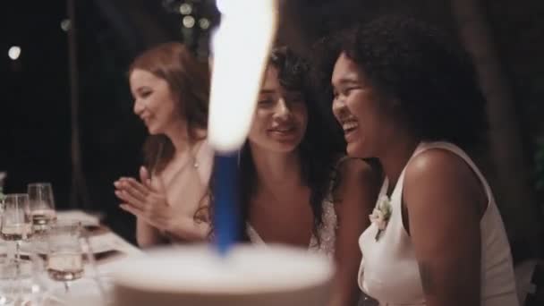 快乐的多种族女同性恋新婚夫妇坐在餐厅的喜庆桌旁 看着装饰着火花的结婚蛋糕 — 图库视频影像