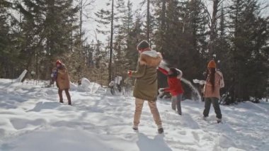 Çok ırklı genç arkadaşların güneşli kış günlerini dışarıda kartopu oynayarak geçirmesi yavaş bir hareket.