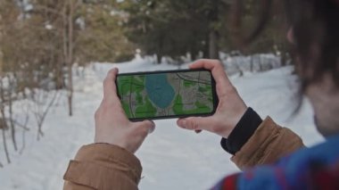 Tanımlanamayan bir adamın elinde akıllı telefon okuma haritası, kış günü gitmek için rota seçerken yakın plan fotoğrafı.