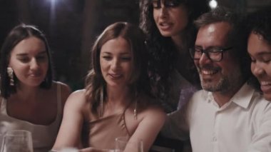 Akşamları modern düğün partisinden zevk alan bir grup insan yemek masasında toplanıp akıllı telefondan fotoğraf izliyorlar.