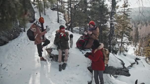 現代の若いアフリカ系アメリカ人と白人の友人の高い角度冬の日に山の中で一緒にハイキングに時間を過ごす彼らの食事を食べるために休憩している — ストック動画