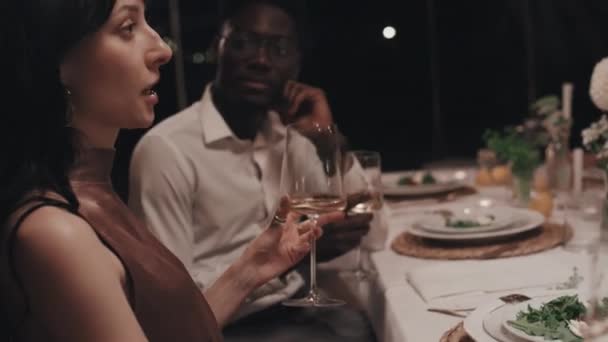 年轻的白人妇女和身穿时髦华丽服装的黑人男子一起在餐馆的节日餐桌边休息 聊天喝酒 — 图库视频影像