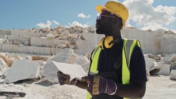 大理石の採石場で働くアフリカ系アメリカ人の男は 周りを見回す紙のシートを保持 — ストック動画