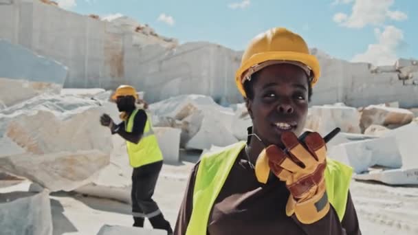 アフリカ系アメリカ人の額装労働者の選択的焦点は 彼女の同僚がバックグラウンドで大理石の石の品質をチェックし Walkie Talkieを使用して採石場労働者と話を身に着けています — ストック動画