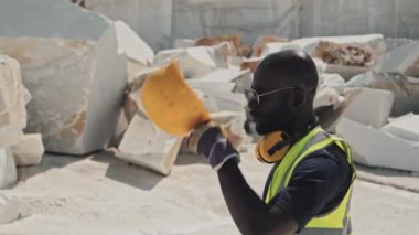 Modern Afrikalı Amerikalı taş ocağı işçisinin ağır çekimde iş kıyafetleri ve güneş gözlüğü takıp bir yerlere yürümesi.