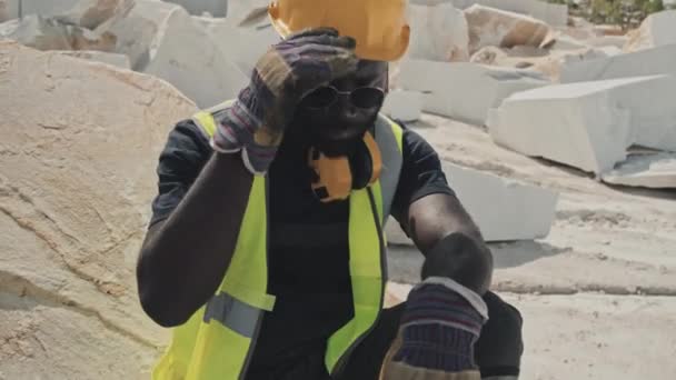 炎热的夏天 穿着工作服的年轻的非洲裔美国人在采石场的大理石石上坐着休息 — 图库视频影像