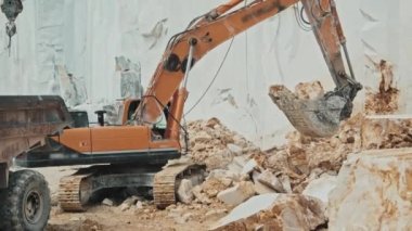 Kamyon kamyonunun açık kutusuna taşları koymak ve taşımak için bumlamayı kontrol eden kazıcı operatörü olarak çalışan tanınmayan kişi