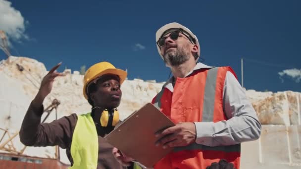 アフリカ系アメリカ人の前女性と成熟した白人の地質学者が大理石の採石場で一緒に作業計画を議論する — ストック動画