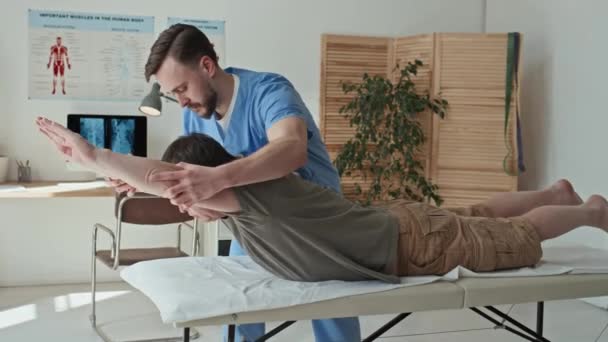 専門の理学療法士が患者に手の練習を示し 医療室のソファで彼を訓練します — ストック動画