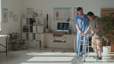 Genç terapist, olgun bir hastanın rehabilitasyonu sırasında Walker 'la yürümesine yardım ediyor.