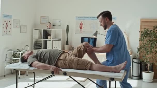 Profesjonalny Fizjoterapeuta Mundurze Wykonujący Ćwiczenia Rozciągające Nogach Pacjenta Leżącego Kanapie — Wideo stockowe