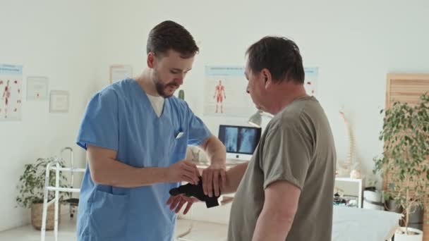 Fizjoterapeuta Mundurze Taśmami Ręce Dojrzałego Pacjenta Kontuzji Podczas Wizyty Szpitalu — Wideo stockowe