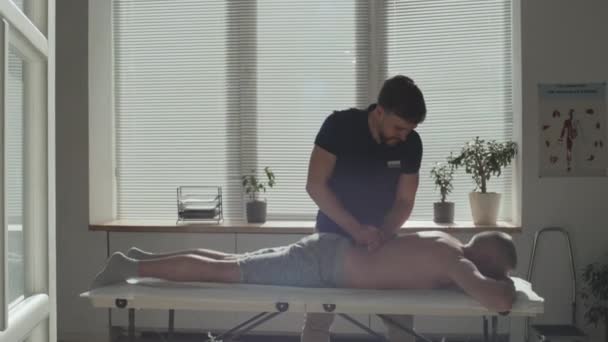 Giovane Terapeuta Massaggiare Schiena Del Paziente Maturo Mentre Rilassa Sul — Video Stock