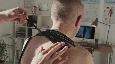 Doktor sırtına tıbbi bant takarken, hastanedeki koltukta oturan kıdemli hastanın dikiz görüntüsü.